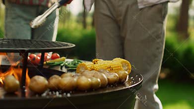 Male chef using forceps for cooking food outdoors. Man hands pouring salt on BBQ
