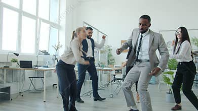 Cheerful young people men and women enjoying dance celebrating company achievement in office