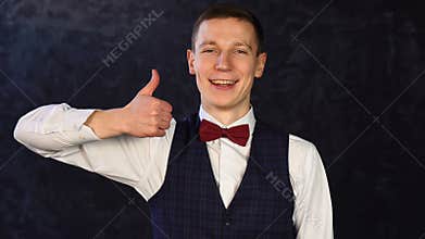 Stylish young man in a vest with a bow-tie with a happy face showing thumb up