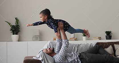 Loving young biracial dad lifting in air little cute daughter.