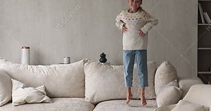 Active carefree little girl jumping on soft sofa at home