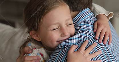 Little daughter and dad cuddling seated on sofa at home