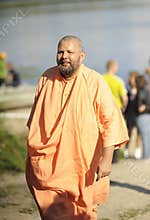 Portrait of the regular Hare Krishna huru dressed in a yellow monk robe, standing on a river beach