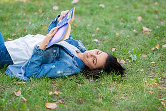 40-year-old woman reading a book in the park. She lies on the grass, reads a book and takes a break from constantly
