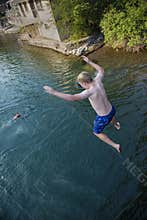 Daring young boy jumping off a bridge into the river. Being adventurous and brave, diving right into the water
