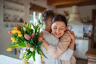 Happy senior mother hugging adult daughter indoors at home, mothers day or birthday celebration.