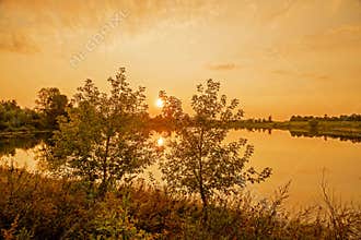 Summer evening in September and a setting sun between the trees over a small lake.