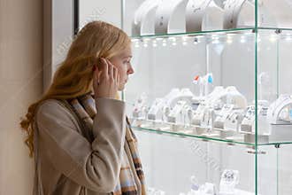 Young woman looking at the shop showcase and jewelry to look at it closer