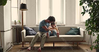 Young foster father tickling on couch with little adopted girl