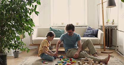 Friendly young dad little daughter play colorful constructor at home