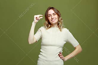 Smiling young girl showing little size gesture with fingers on green background. Small prices, shopping sales discount