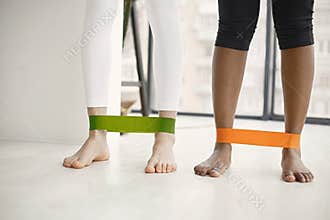 Cropped photo of black and caucasian women standing in studio with fitness rubber on legs