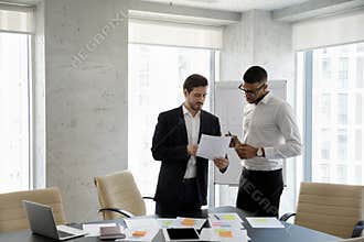 Multiethnic businessmen consider documents, share information working in boardroom