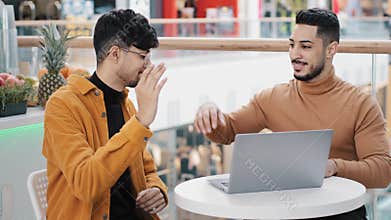 Happy young guys friends sitting in cafe arab man showing on laptop achievement new project great result indian man
