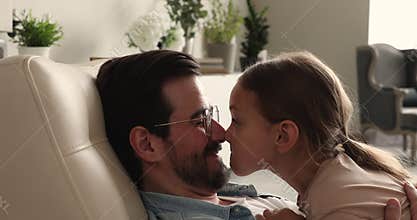 Little daughter her father touch noses laughing resting on armchair