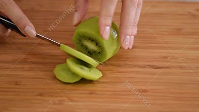 Hands womens cut fresh kiwi into thin round slices.