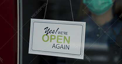small business owner with face mask reopen closed shop after covid-19 pandemic. turning open sign