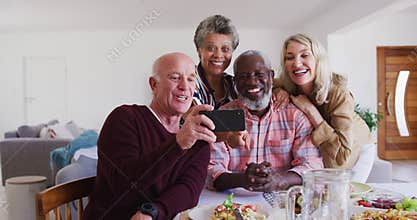 Diverse senior couples sitting by a table drinking wine eating dinner and taking a selfie