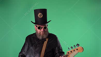A bearded man in a long leather coat, an Irish style hat and original glasses plays the red guitar. Rock musician plays