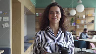 Happy latin girl student holding coffee walking in campus hallway.