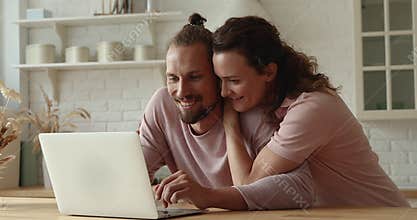 Happy bonding affectionate young couple using computer at home.