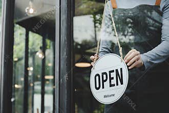 Asian waitress staff woman wearing apron turning open sign board on glass door in modern cafe coffee shop, hotel, cafe restaurant,