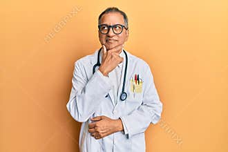 Middle age indian man wearing doctor coat and stethoscope with hand on chin thinking about question, pensive expression