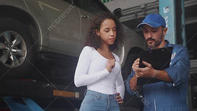 Young mechanic stand and talking to customer about car with repairing in the garage, auto service.