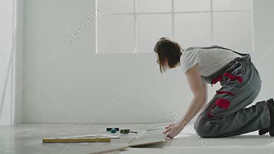 Woman builder with dark hair lays laminate plate on floor