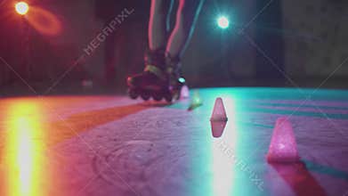 Close-up of teenager legs roller skating around obstacles in slow motion. Millennial showing trick freeskating in dark