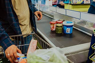 man lays out groceries from supermarket basket on conveyor belt. Shopping foods, cash register in store.