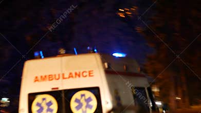 An ambulance car with flashing beacons on rushes down a city street at night