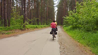 Two young men with backpacks ride bicycles along the road.