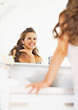 Happy woman looking in mirror in bathroom
