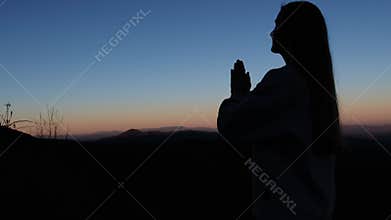A woman prays at sunset, finding peace in natures beauty