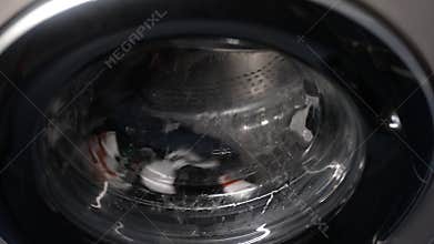 Everyday chore of laundry - washing machine drum spinning with socks and laundry detergent inside, providing glimpse