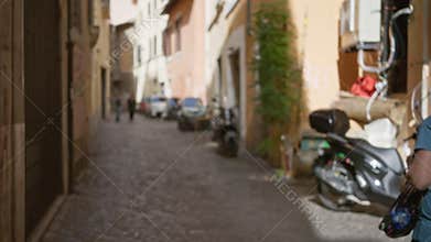 Blurry pedestrian street in rome with defocused architecture featuring vibrant hues and parked scooters