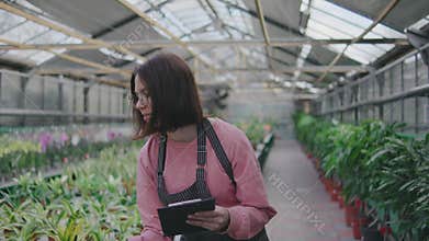 Portrait of a female greenhouse worker. A girl holds a writing tablet in her hands. Woman writes something in a notebook