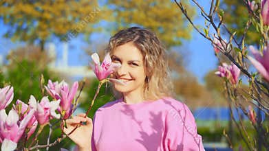 Portrait blond hair happy woman touches pink magnolia flower, blossoming tree branch. Beauty girl smiling joyful face