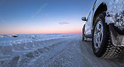 Perspective wheel of icy 4x4 car on a totally snowy road with tire tracks that goes all the way to the horizon.