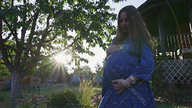 Beautiful pregnant woman enjoying fresh air at sunset rays on the backyard