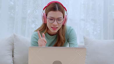 Young asian woman enjoy music while wearing headphones and working on laptop computer in living room.