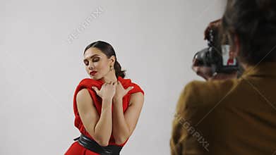 Model and production team in the studio. Close up shot of appealing brunette woman model in red dress posing for camera.