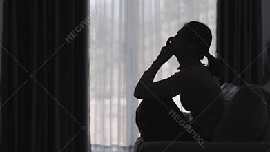 Silhouette of a person suffering from depression in the house, depressed woman sitting alone on the sofa feel stress, sad and