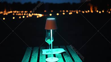 An empty table with a lit lamp, evening rain. On the table, an empty glass of a consumed cocktail. Blurred background