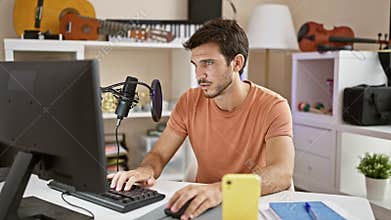Hispanic man with beard in a music studio using a computer and microphone for podcasting
