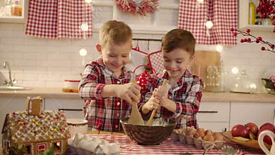 Cute boys making gingerbread dough together at the kitchen on Christmas eve