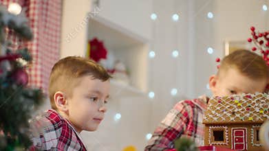 Cute boys decorating gingerbread house with topping and icing at the kitchen