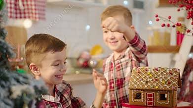 Cute boys decorating gingerbread house with topping and icing at the kitchen
