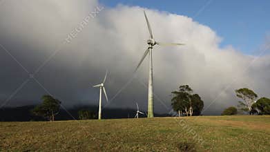 Wind turbines turning in the sunshine while a storm brews in the background